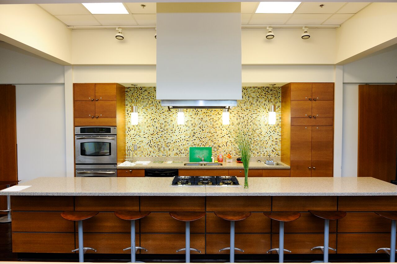 Image of a kitchen with a stove and sink in the background and a countertop and cooking range in the foreground